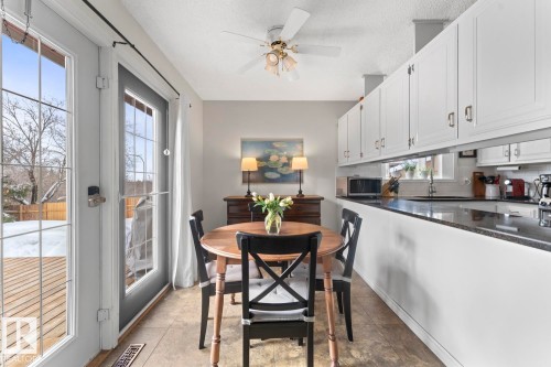 Bright dining area featuring a ceiling fan, direct access to the outdoor deck, and a view of the kitchen with white cabinetry and dark countertops - 4003 50A Avenue, Cold Lake, AB - Indoor