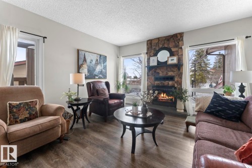 Living area featuring wood-look flooring, a stone fireplace, and large windows offering views of the outdoors - 4003 50A Avenue, Cold Lake, AB - Indoor Photo Showing Living Room With Fireplace
