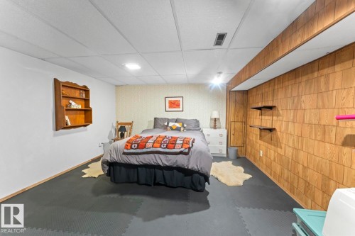 This versatile room features a drop ceiling with recessed lighting, two distinct wall finishes, and dark grey interlocking floor tiles - 4003 50A Avenue, Cold Lake, AB - Indoor Photo Showing Bedroom