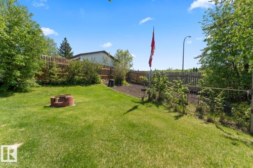 Expansive green lawn with a built-in fire pit, surrounded by mature trees and a wood privacy fence - 4003 50A Avenue, Cold Lake, AB - Outdoor