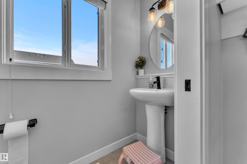 Bathroom featuring a pedestal sink, black faucet, and a round mirror with an overhead vanity light - 6406 169 Avenue, Edmonton, AB - Indoor Photo Showing Bathroom