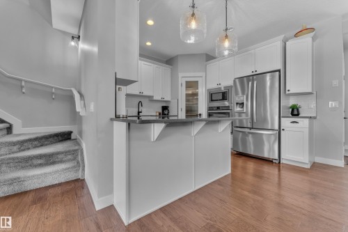 The kitchen features white cabinetry, stainless steel appliances, and a breakfast bar with pendant lighting - 6406 169 Avenue, Edmonton, AB - Indoor Photo Showing Kitchen With Stainless Steel Kitchen With Upgraded Kitchen