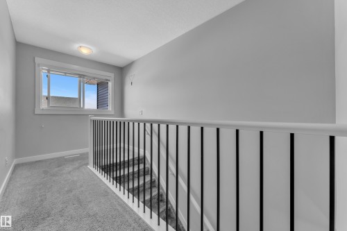 This property features a landing area with light grey carpet, a white framed window providing natural light, and a staircase with a white railing and black balusters - 6406 169 Avenue, Edmonton, AB - Indoor Photo Showing Other Room