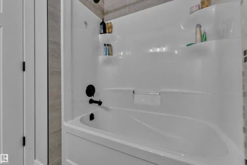 Bathroom featuring a white bathtub with dark fixtures and light grey tiled walls - 6406 169 Avenue, Edmonton, AB - Indoor Photo Showing Bathroom