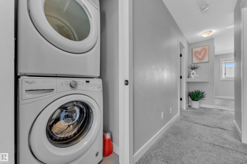 Dedicated laundry area featuring a white stacked washer and dryer, with a light gray carpeted hallway - 6406 169 Avenue, Edmonton, AB - Indoor Photo Showing Laundry Room