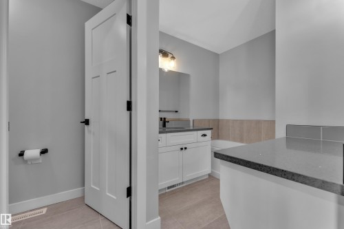 This bathroom features a contemporary vanity with a dark countertop and a white cabinet, a built-in bathtub, and light-toned wall tiles - 6406 169 Avenue, Edmonton, AB - Indoor