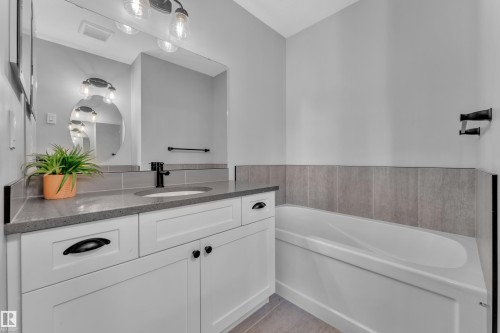 Bathroom featuring a vanity with white cabinetry, a dark countertop, and an undermount sink with a black faucet - 6406 169 Avenue, Edmonton, AB - Indoor Photo Showing Bathroom