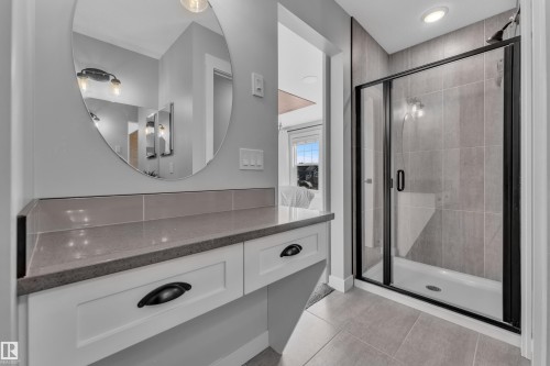 The bathroom features a vanity with a countertop and drawers, an oval mirror, and a shower with a clear glass enclosure and dark frame - 6406 169 Avenue, Edmonton, AB - Indoor Photo Showing Bathroom