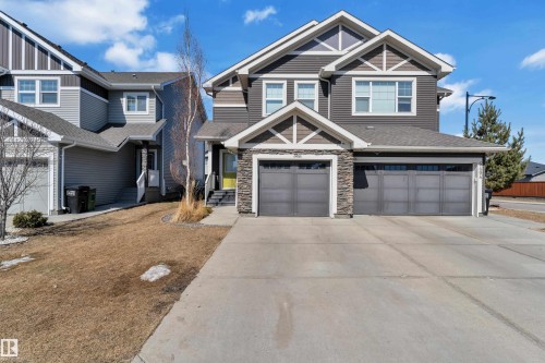 The property features a two-story exterior with dark siding and stone accents, a prominent front entrance with a bright yellow door, and a large concrete driveway leading to two garage doors - 6406 169 Avenue, Edmonton, AB - Outdoor With Facade