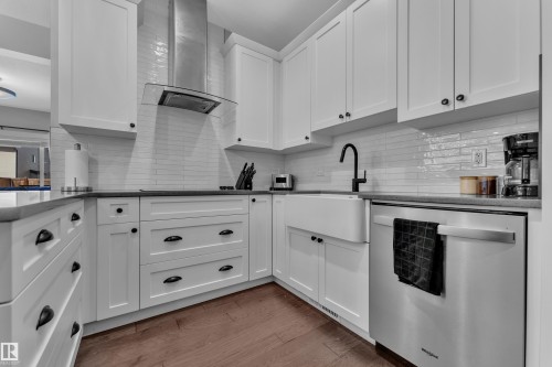 Contemporary kitchen featuring white cabinetry, dark countertops, a farmhouse sink, stainless steel appliances, and wood flooring - 6406 169 Avenue, Edmonton, AB - Indoor Photo Showing Kitchen With Upgraded Kitchen