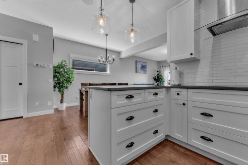 The kitchen features white cabinetry with dark hardware, dark countertops, and a white subway tile backsplash, complemented by hardwood flooring - 6406 169 Avenue, Edmonton, AB - Indoor