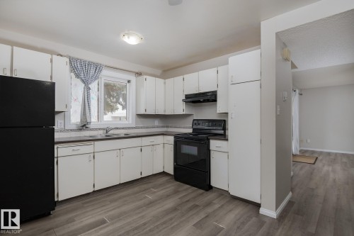 The kitchen features white cabinetry, a window providing natural light, and modern black appliances including a refrigerator, oven, and range hood - 37 Woodvale Village, Edmonton, AB - Indoor Photo Showing Kitchen With Double Sink