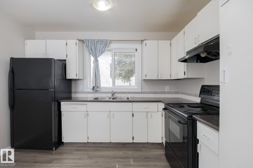 The kitchen features white cabinetry, a double basin sink, and black appliances including a refrigerator and an electric range with an overhead exhaust fan - 37 Woodvale Village, Edmonton, AB - Indoor Photo Showing Kitchen With Double Sink
