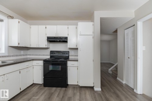 Well-appointed kitchen featuring white cabinetry, a black oven and range hood, dark countertops, and a tiled backsplash - 37 Woodvale Village, Edmonton, AB - Indoor Photo Showing Kitchen