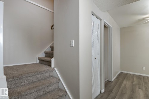 This interior features a carpeted staircase with a handrail, a louvered bi-fold door, and wood-look flooring - 37 Woodvale Village, Edmonton, AB - Indoor Photo Showing Other Room