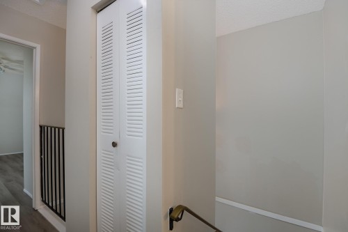 Hallway featuring white louvered bifold doors, a light-colored wall with white trim, and a black metal railing - 37 Woodvale Village, Edmonton, AB - Indoor Photo Showing Other Room
