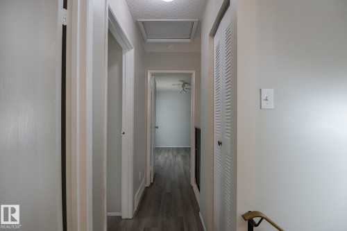 The hallway features light-colored walls and dark flooring, with a visible ceiling hatch and a closet with louvered doors - 37 Woodvale Village, Edmonton, AB - Indoor