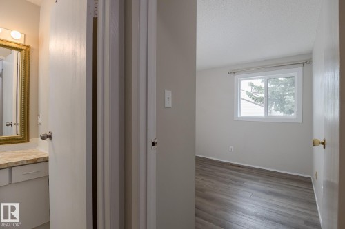 Well-maintained interior featuring a vanity with a mirror and overhead lighting, alongside a room with wood-style flooring and a window - 37 Woodvale Village, Edmonton, AB - Indoor Photo Showing Other Room