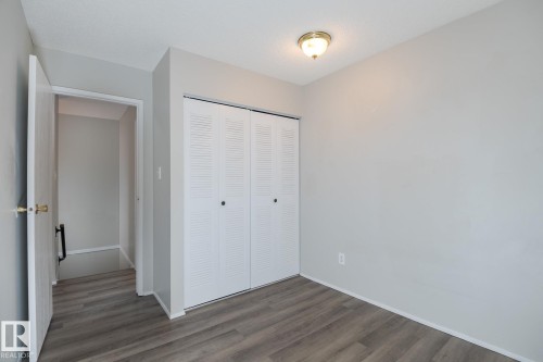 This room features light grey walls, wood-style flooring, a ceiling light fixture, and white bi-fold closet doors - 37 Woodvale Village, Edmonton, AB - Indoor Photo Showing Other Room