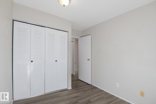 This room features wood-look flooring, a closet with bi-fold louvered doors, and a ceiling-mounted light fixture - 37 Woodvale Village, Edmonton, AB - Indoor Photo Showing Other Room