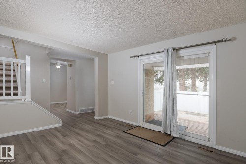 This property features a bright living area with wood-look flooring and a sliding glass door leading to an outdoor deck - 37 Woodvale Village, Edmonton, AB - Indoor Photo Showing Other Room
