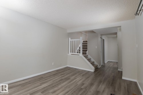The living area features light-toned walls, hardwood style flooring, and a staircase with white railings - 37 Woodvale Village, Edmonton, AB - Indoor Photo Showing Other Room