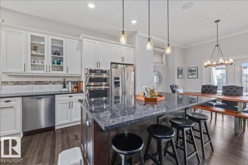 Open-concept kitchen featuring white cabinetry, stainless steel appliances, a dark granite island with pendant lighting, and hardwood flooring - 3908 Ginsburg Crescent, Edmonton, AB - Indoor Photo Showing Kitchen With Upgraded Kitchen