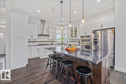 Modern kitchen featuring white cabinetry, dark countertops, a large center island with seating, stainless steel appliances, and dark wood flooring - 3908 Ginsburg Crescent, Edmonton, AB - Indoor Photo Showing Kitchen With Upgraded Kitchen
