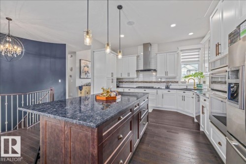Well-appointed kitchen featuring white cabinetry, stainless steel appliances, a large island with a dark countertop, and dark wood flooring - 3908 Ginsburg Crescent, Edmonton, AB - Indoor Photo Showing Kitchen With Upgraded Kitchen