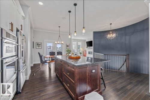 The open concept main living area features dark wood flooring, a kitchen island with a granite countertop, and stainless steel appliances - 3908 Ginsburg Crescent, Edmonton, AB - Indoor Photo Showing Kitchen With Upgraded Kitchen