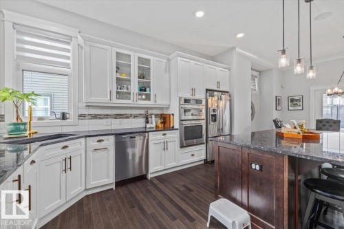 The kitchen features white cabinetry, stainless steel appliances, dark granite countertops, and dark wood flooring - 3908 Ginsburg Crescent, Edmonton, AB - Indoor Photo Showing Kitchen With Upgraded Kitchen