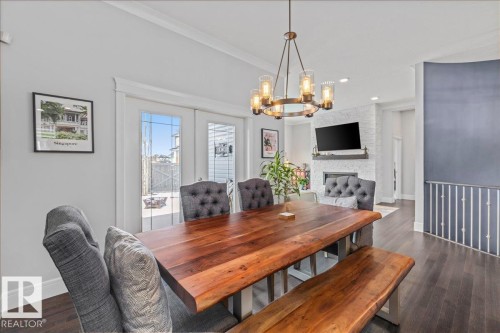This dining area features dark hardwood flooring, a modern chandelier, and access to the outdoors via double french doors - 3908 Ginsburg Crescent, Edmonton, AB - Indoor Photo Showing Dining Room With Fireplace