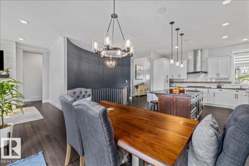 The property features hardwood floors, a modern kitchen with white cabinetry and a large island, and a dining area with a contemporary chandelier - 3908 Ginsburg Crescent, Edmonton, AB - Indoor Photo Showing Dining Room