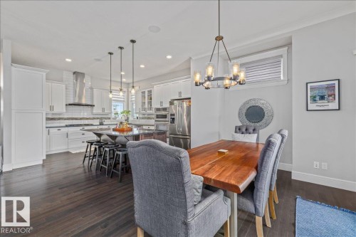 Open concept kitchen and dining area with dark hardwood floors, white cabinetry, a large kitchen island with pendant lighting, and stainless steel appliances - 3908 Ginsburg Crescent, Edmonton, AB - Indoor Photo Showing Dining Room