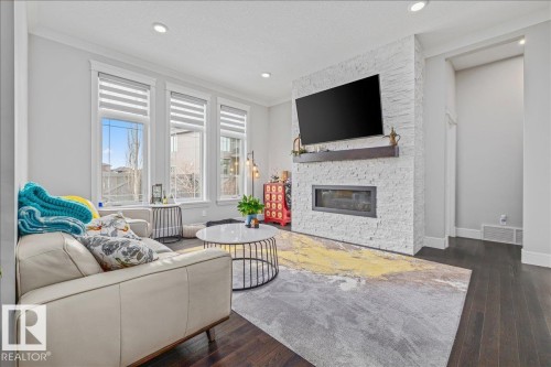 Living area featuring dark hardwood floors, recessed lighting, and large windows providing natural light - 3908 Ginsburg Crescent, Edmonton, AB - Indoor Photo Showing Living Room With Fireplace