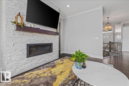 The living area features a white stacked stone fireplace with a dark wood mantel and a rectangular firebox, complemented by dark wood flooring and light gray walls - 3908 Ginsburg Crescent, Edmonton, AB - Indoor Photo Showing Living Room With Fireplace