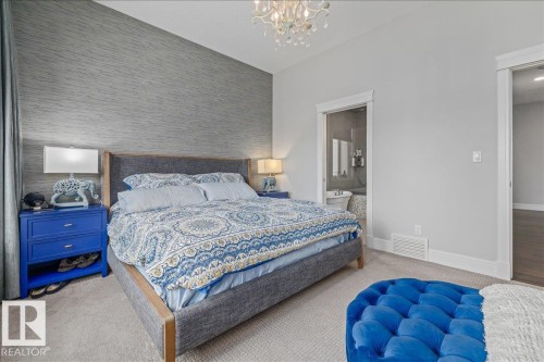 Bedroom featuring a patterned accent wall, light grey carpet, and a decorative chandelier - 3908 Ginsburg Crescent, Edmonton, AB - Indoor Photo Showing Bedroom
