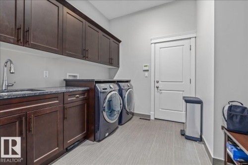 The utility room features extensive dark wood cabinetry, a sink with a chrome faucet, and dark granite countertops - 3908 Ginsburg Crescent, Edmonton, AB - Indoor Photo Showing Laundry Room