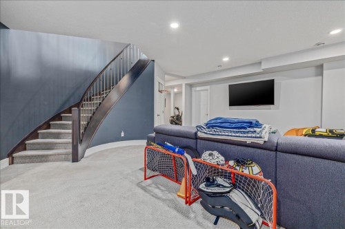 This recreation room features light-colored carpeting, a wall-mounted television, and recessed lighting - 3908 Ginsburg Crescent, Edmonton, AB - Indoor Photo Showing Other Room