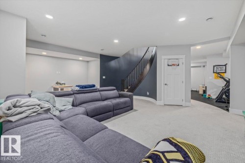 Carpeted room with recessed lighting and a stairway featuring dark wood banisters and a dark blue accent wall - 3908 Ginsburg Crescent, Edmonton, AB - Indoor