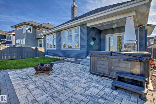 This property features a spacious paved patio area, a hot tub, and a fire pit, all set against a backdrop of a fenced yard with a lawn - 3908 Ginsburg Crescent, Edmonton, AB - Outdoor