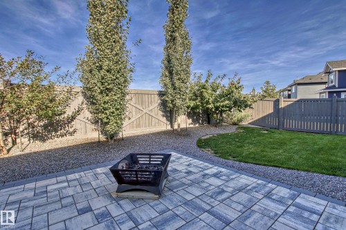 The property features a paved patio area with a fire pit, a gravel pathway, a lawn, and a wooden fence - 3908 Ginsburg Crescent, Edmonton, AB - Outdoor
