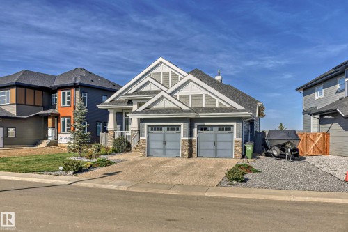 The property features a two-car garage with grey doors, a paved driveway, and a well-maintained lawn with landscaping - 3908 Ginsburg Crescent, Edmonton, AB - Outdoor With Facade