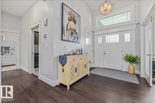 The inviting entryway features dark wood flooring, a white front door with decorative glass panels and a transom window, and a stylish chandelier - 3908 Ginsburg Crescent, Edmonton, AB - Indoor Photo Showing Other Room