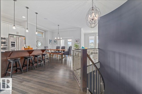 This expansive open-concept area features dark hardwood flooring throughout, a kitchen island with pendant lighting, and a dining area with a modern chandelier - 3908 Ginsburg Crescent, Edmonton, AB - Indoor