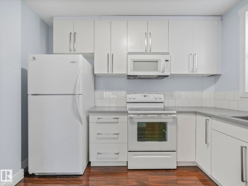 The kitchen features white cabinetry, a white refrigerator, a white oven with a stovetop, and a white microwave above the oven - 12141 96 Street, Edmonton, AB - Indoor Photo Showing Kitchen