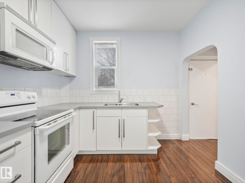 The kitchen features white cabinetry, white appliances, a stainless steel sink, and a tiled backsplash - 12141 96 Street, Edmonton, AB - Indoor Photo Showing Kitchen With Double Sink