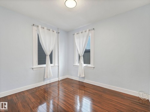 This room features lustrous wood flooring, light-colored walls, and two windows adorned with sheer white curtains - 12141 96 Street, Edmonton, AB - Indoor Photo Showing Other Room