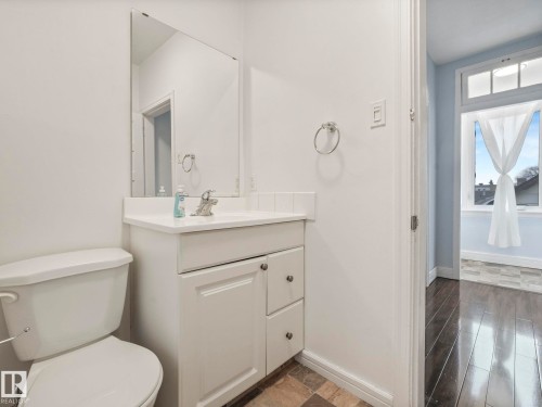 This bathroom features a white vanity with a countertop sink, a wall-mounted mirror, and a toilet - 12141 96 Street, Edmonton, AB - Indoor Photo Showing Bathroom