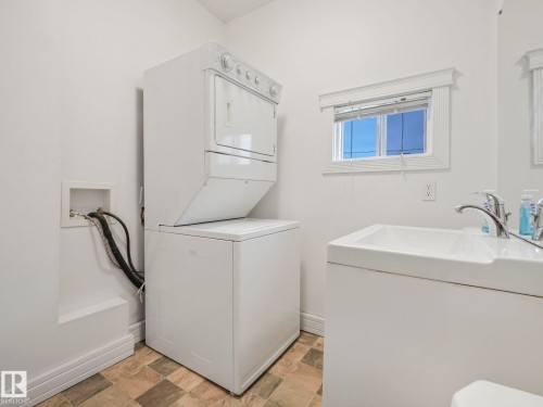 This utility area features a stackable washer and dryer, a window with blinds, and a vanity with a sink and faucet - 12141 96 Street, Edmonton, AB - Indoor Photo Showing Laundry Room